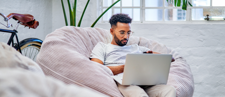Image of man sitting on a couch looking at his laptop to update his talent profile.